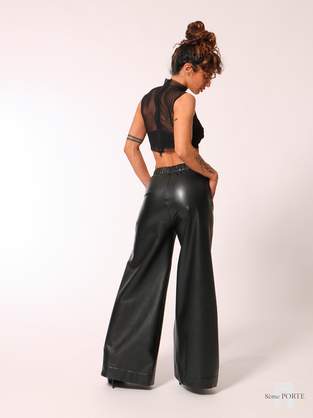 Back view of custom-made faux leather wide-leg joggers with hands on hips, styled with high heels to emphasize the elongated silhouette and dramatic drape.