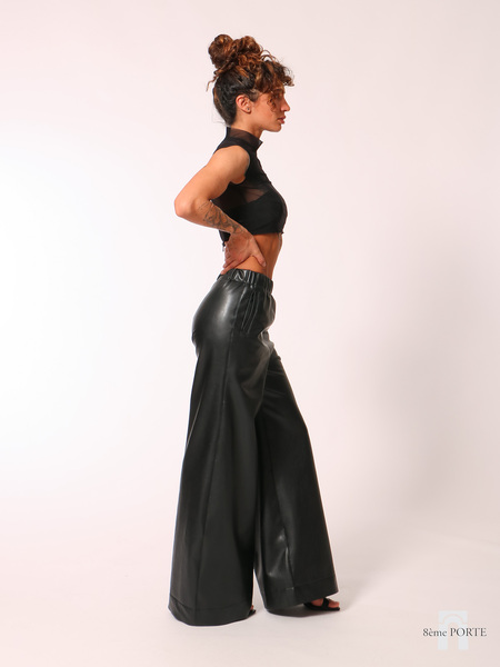 Side profile view of custom wide-leg faux leather trousers with hand on hip, styled elegantly with high heels to showcase the long, floor-sweeping drape.