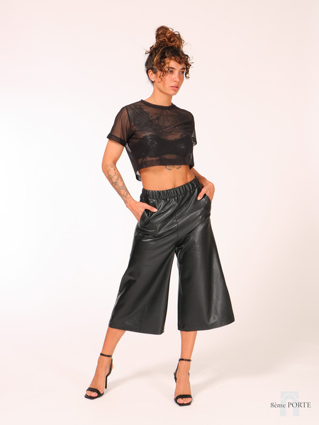Front view of model wearing 8ÈME PORTE black faux leather culottes styled with a mesh top and strappy heels.
