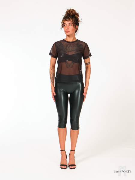 Full front view of model wearing the loose fit black mesh t-shirt layered over a bandeau bra with high-waisted Flora faux leather capri pants.