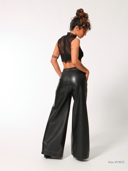 Back view of custom-made faux leather wide-leg joggers with hands on hips, styled with high heels to emphasize the elongated silhouette and dramatic drape.
