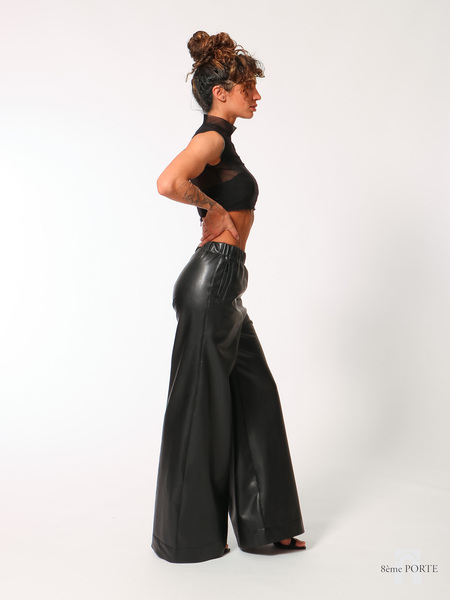 Side profile view of custom wide-leg faux leather trousers with hand on hip, styled elegantly with high heels to showcase the long, floor-sweeping drape.